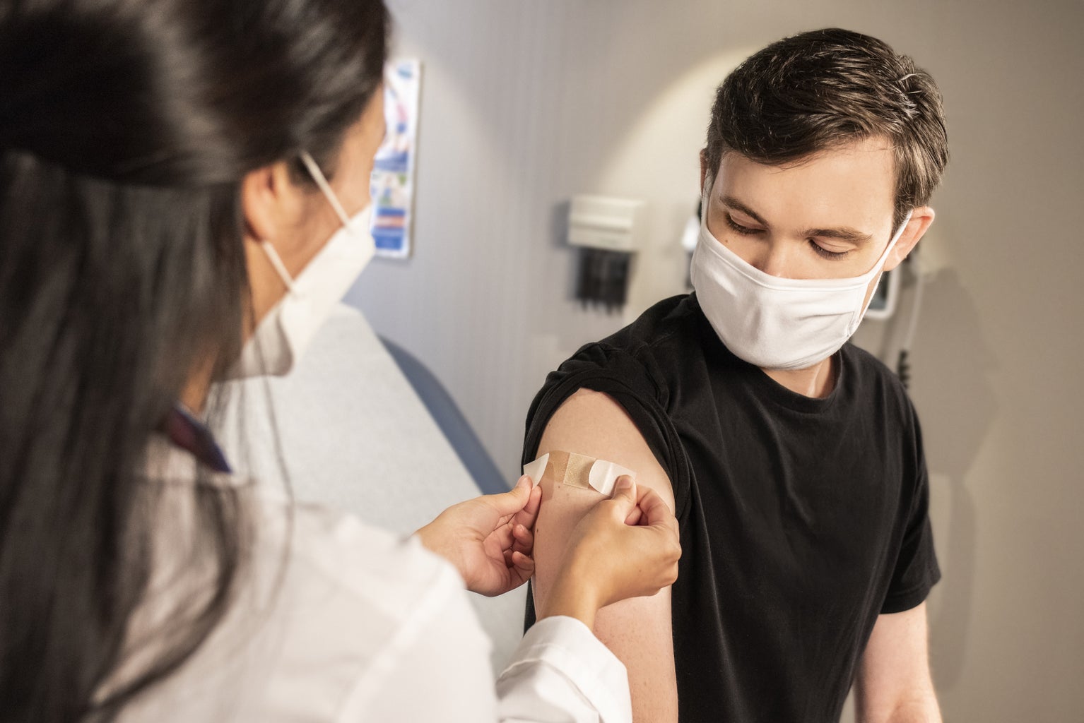 masked doctor applying a bandaid to the arm of a masked patient