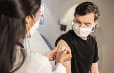 masked doctor applying a bandaid to the arm of a masked patient