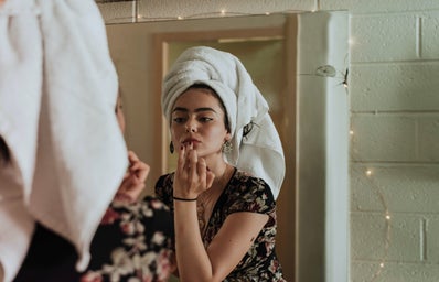 Woman putting lipstick on, a towel on her head.