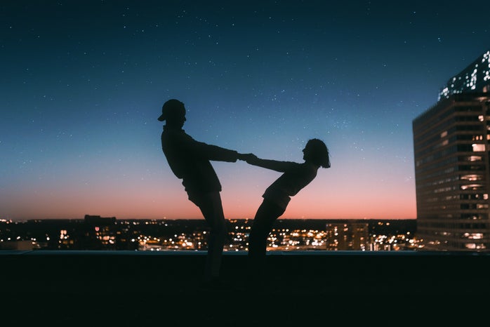 silhouette of people holding hands at sunset and leaning away from each other
