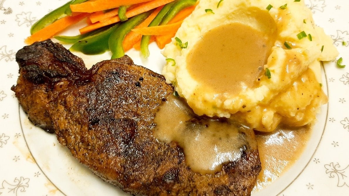 plate of mashed potatoes with gravy, vegetables, and steak