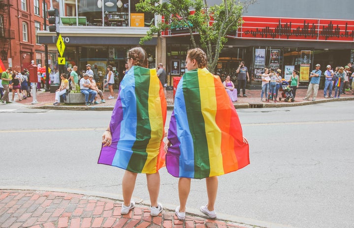 Two people wearing LGBTQ pride flags