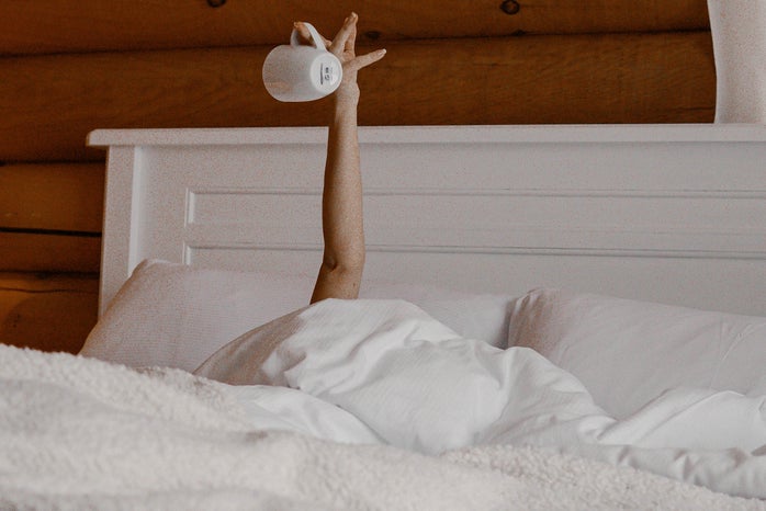 Woman reaching up with an empty cup of coffee in bed.