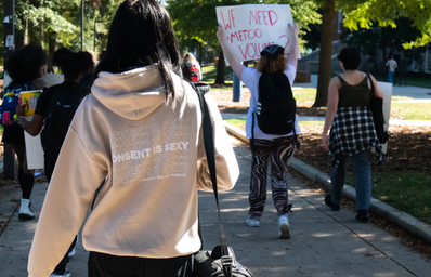 A girl walks in a protest, her hoodie says consent is sexy