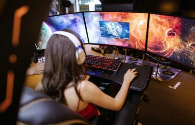 A woman with headphones in front of a three-monitor computer.