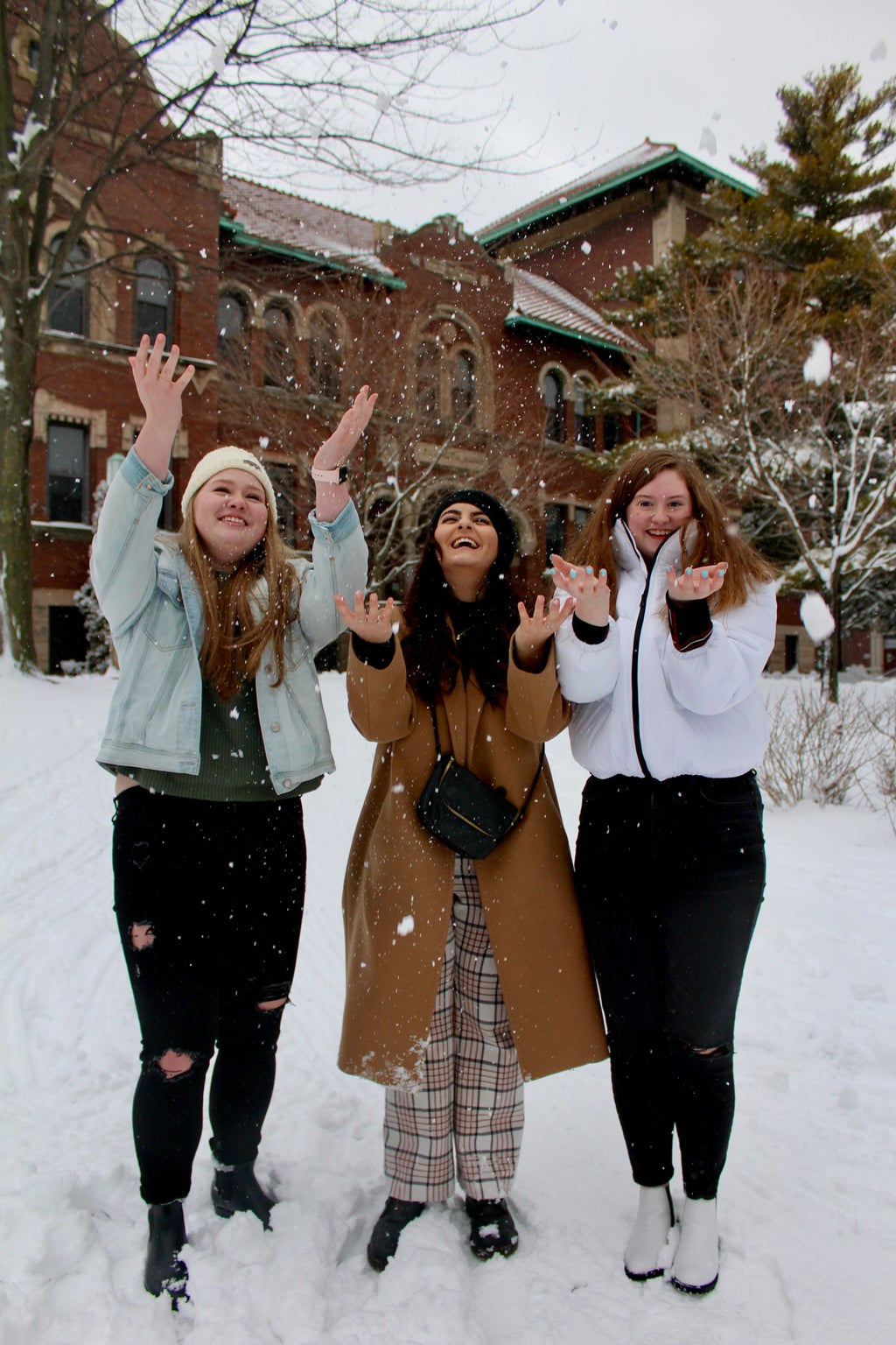 Three women throwing snow in the air on campus