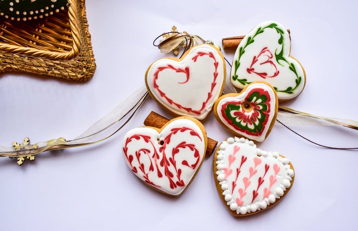 Five holiday sugar cookies all in the shape of a heart with various Christmas décor around it