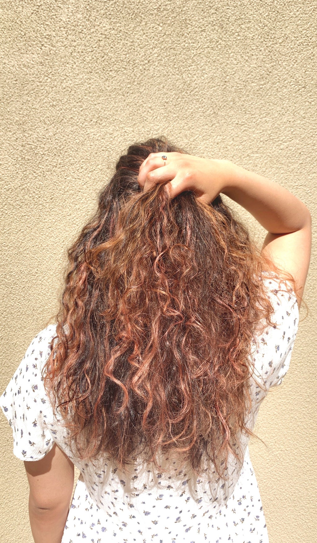 A woman runs her hands through her hair while facing away from the camera