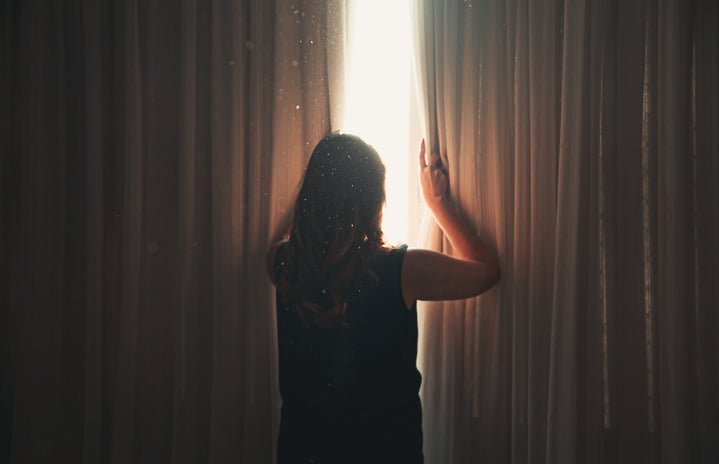 woman opening window curtain in shining daylight