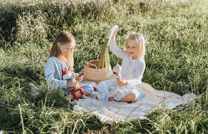 Two girls playing with dolls on a picnic blanket