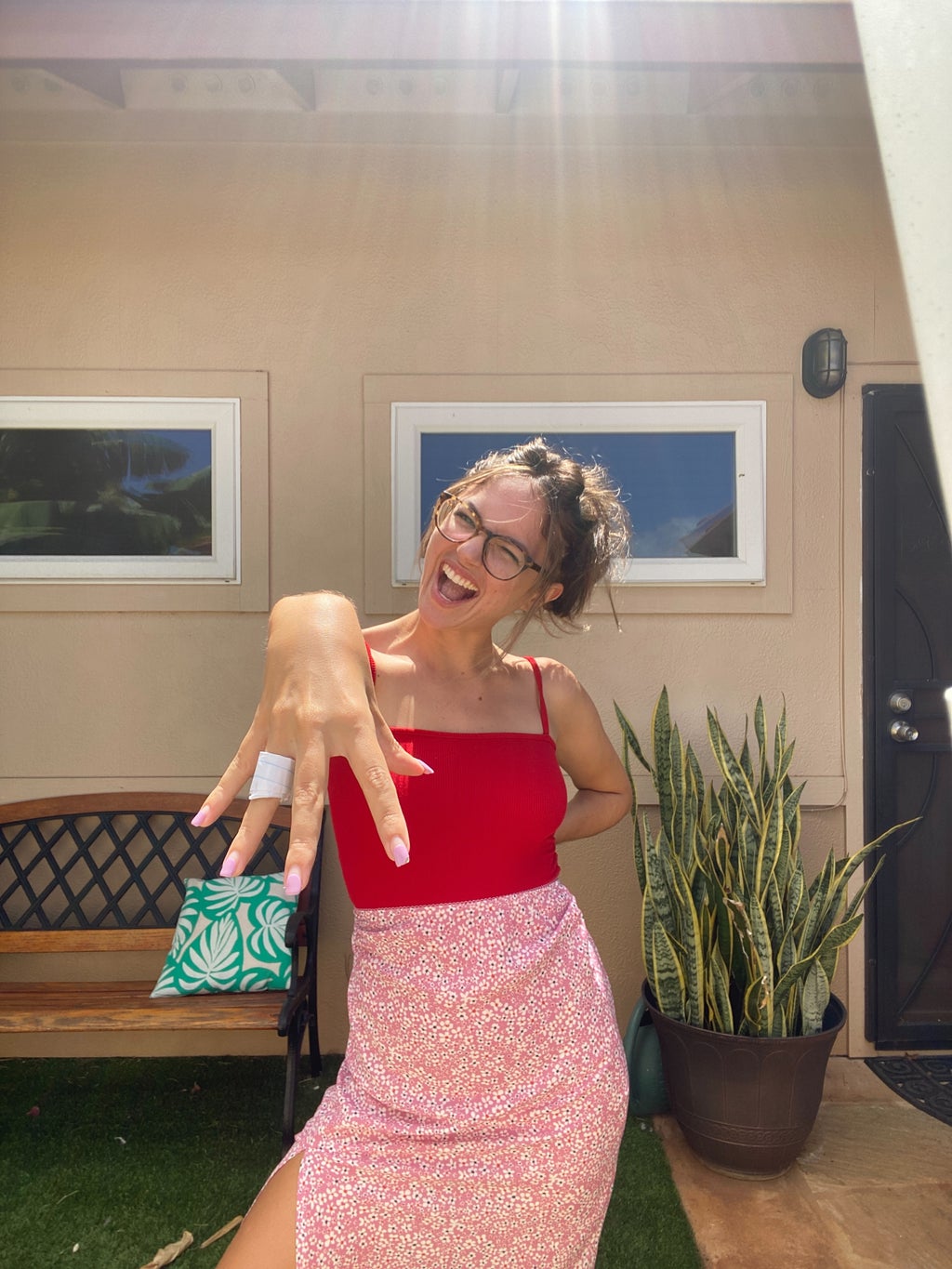Woman posing in a red top, pink shirt, with a hand near the camera.