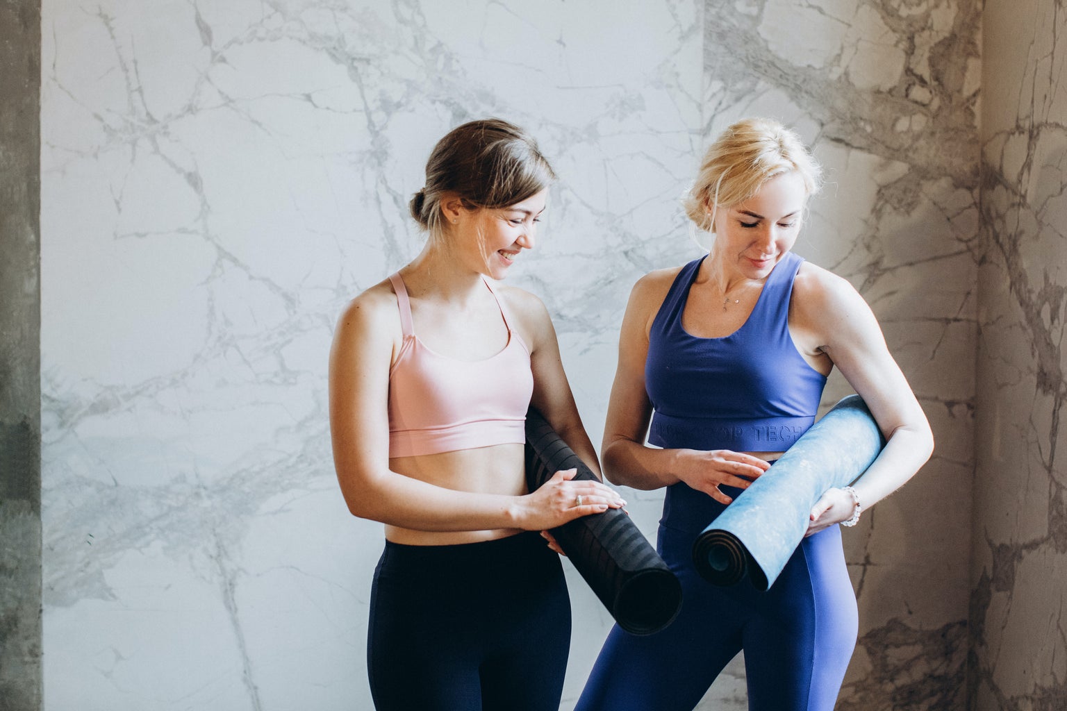 Two women in leggings holding yoga mats