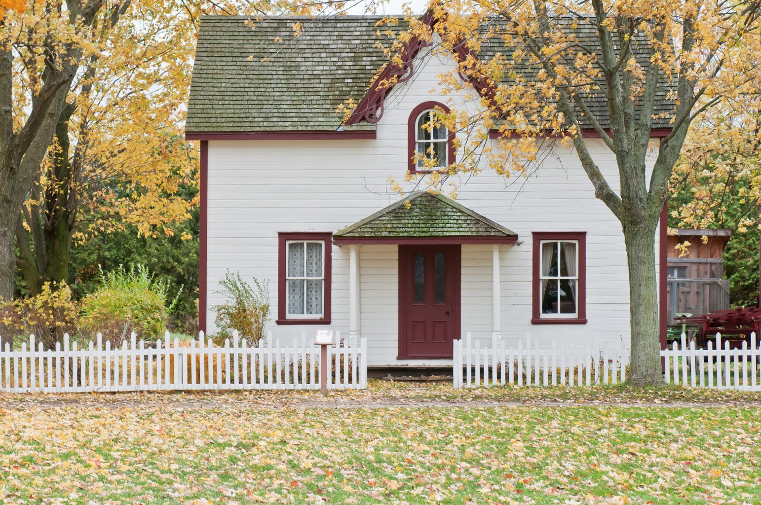 Small house on an autumn’s day. The house is white and there are bare trees in front of it.