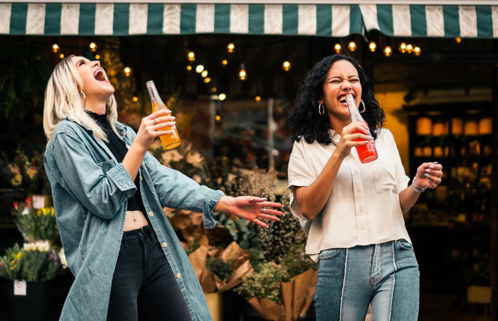 Women in denim laughing as they drink outside a restaurant