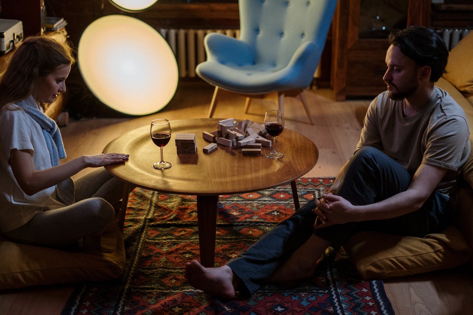 A couple sitting at a table with two glasses of wine playing Jenga. The blocks are knocked over.