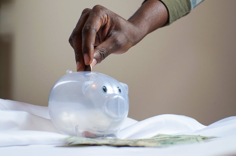 Hand inserting coin into plastic piggy bank