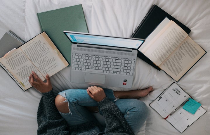 Woman sitting on bed with laptop and books