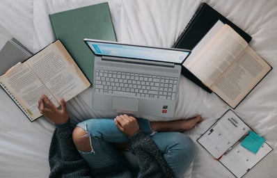 Woman sitting on bed with laptop and books
