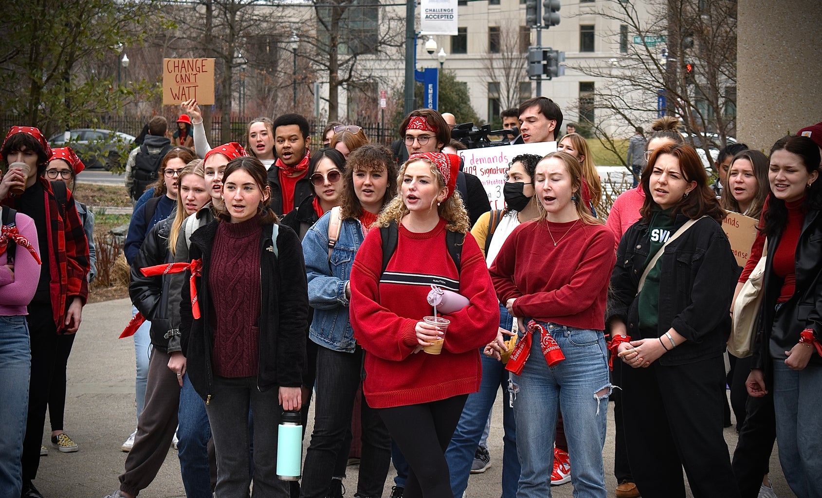 A small crowd of college students, many wearing red, in the midst of a chant supporting sexual assault survivors.