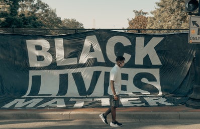 Black Lives Matter sign with man walking in front of it