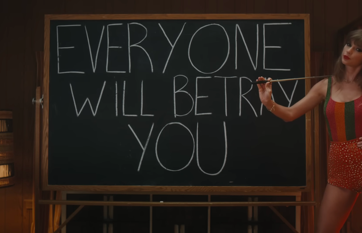 Swift standing in front of chalkboard that reads \"Everybody will betray you\"