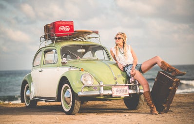 woman with suitcase on beach with vw beetle