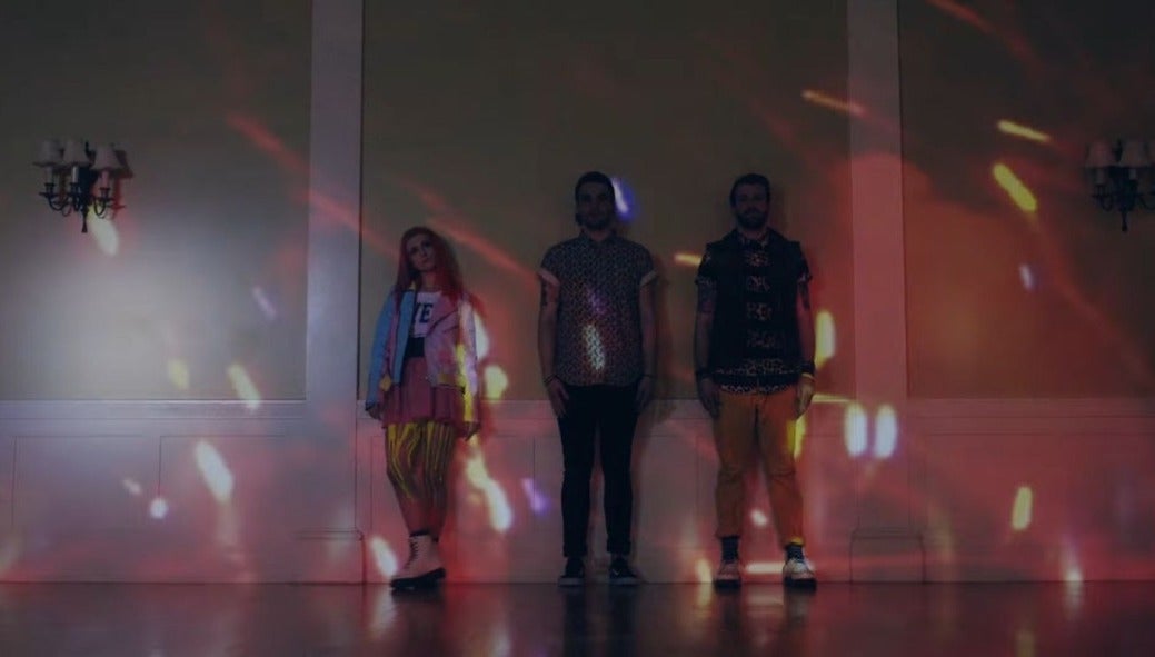 Os membros da banda Paramore posam em um salão de dança vazio, e por mais que seja muito mais colorido que os outros clipes, a postura dos integrantes traz a mesma identidade de sempre./ Foto: Isaac Rentz via YouTube