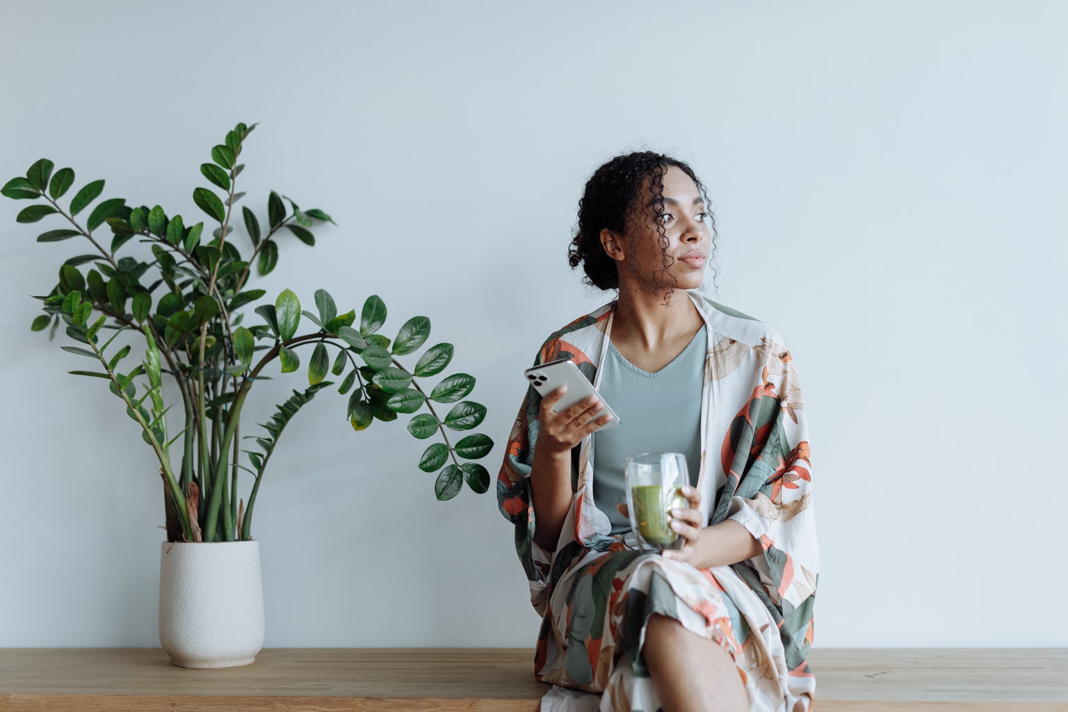 A woman holds her phone and drinks matcha.