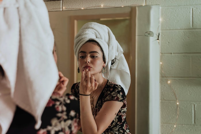 Woman with a towel on her head applying lipstick.