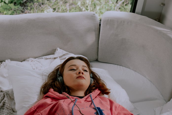 girl lying on a white bed, with headphones on, staring blankly