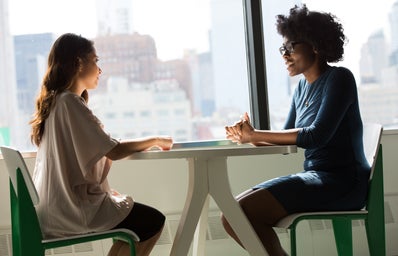 Two women sit at a table and talk