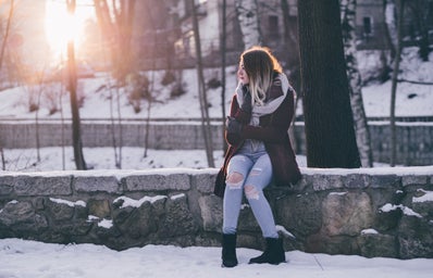 woman in winter clothing is sitting outside in the snow