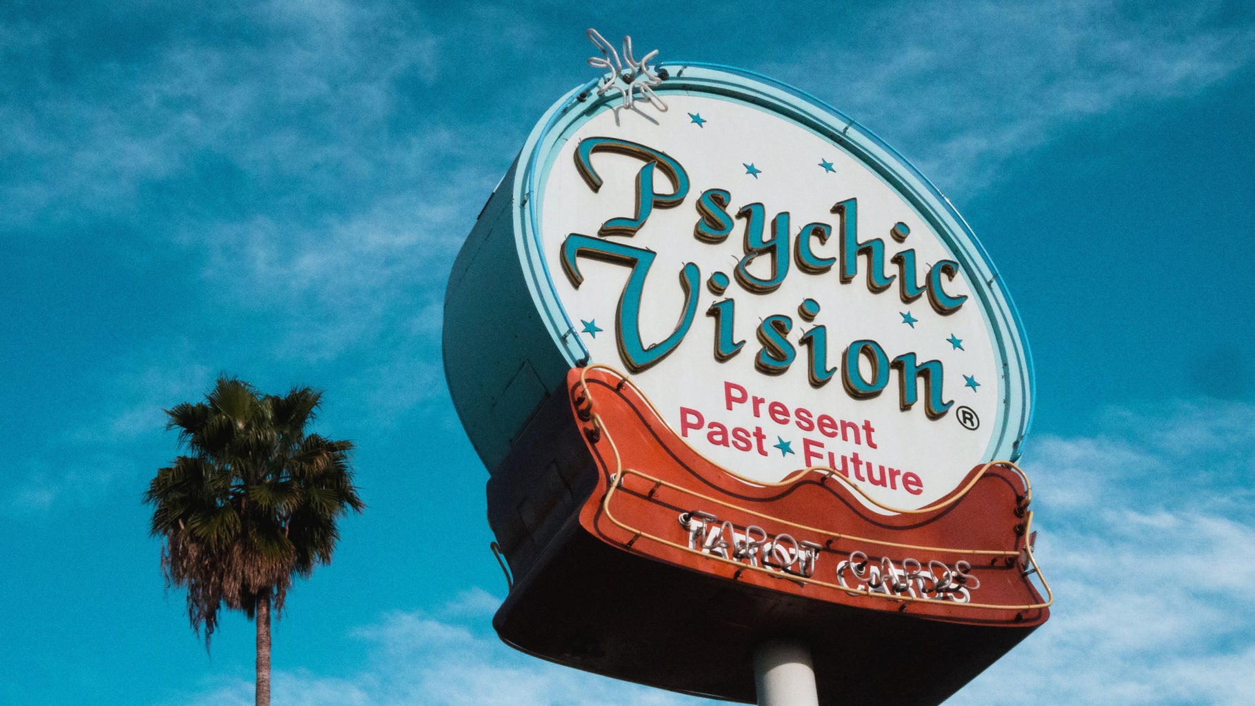 A blue, white and red \'Psychic Vision, Present Past Future, Tarot Cards\' sign with a palm tree in the background