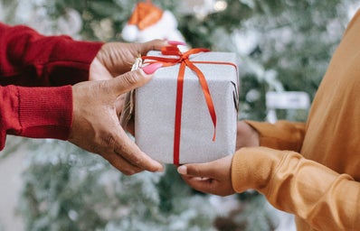 woman handing gift to child in front of christmas tree