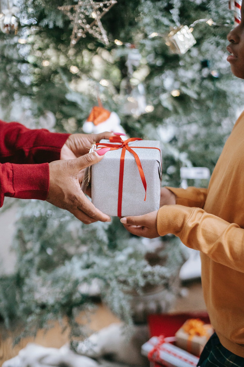 woman handing gift to child in front of christmas tree