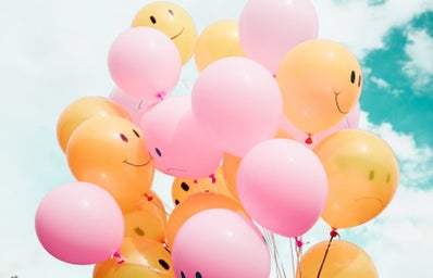 multiple yellow and pink balloons, some with smiles and frowns on them