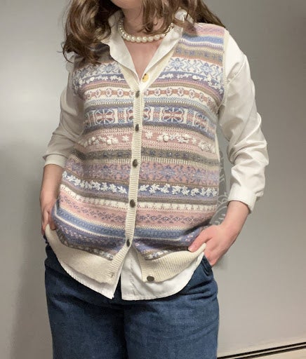 Woman wearing purple, blue and white sweater vest with pearl necklace.