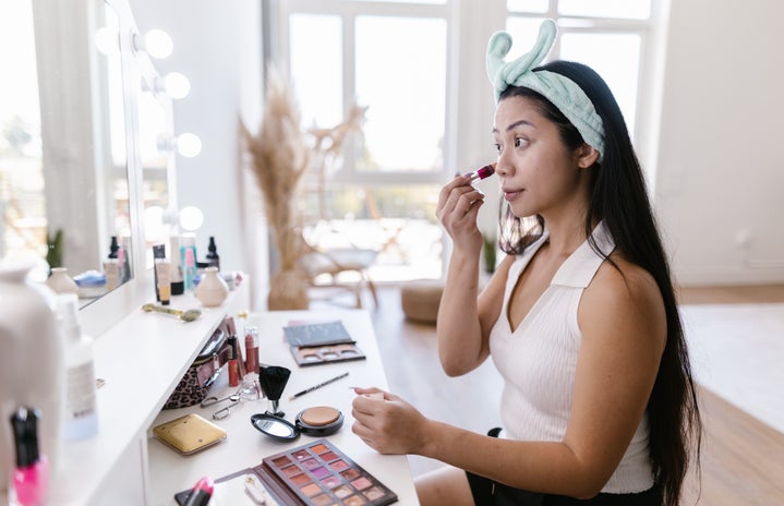 A woman sitting in front of a vanity doing her makeup