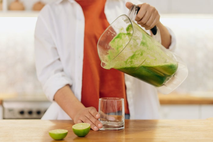person pouring green smoothie into a glass
