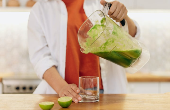 person pouring green smoothie into a glass