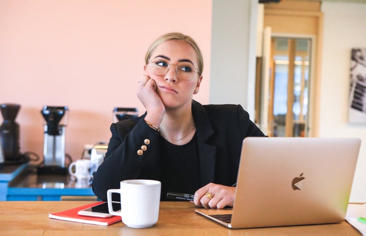 Woman sitting at desk with laptop and coffee looking bored