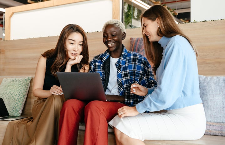 Multiracial cheerful women browsing laptop together