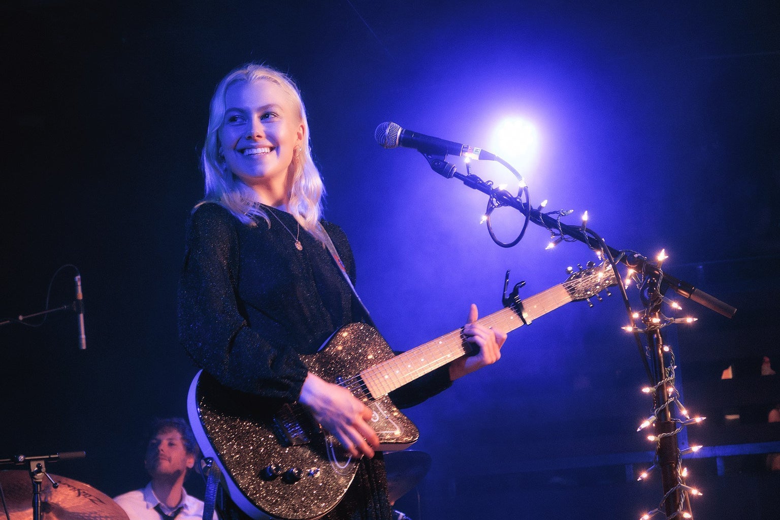 Phoebe Bridgers at the mic with her guitar, playing a live show.