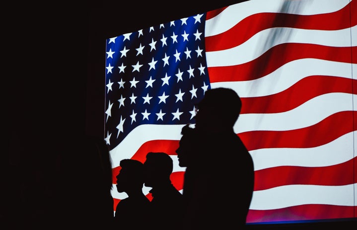 Four silhouettes stand in front of a digital American flag