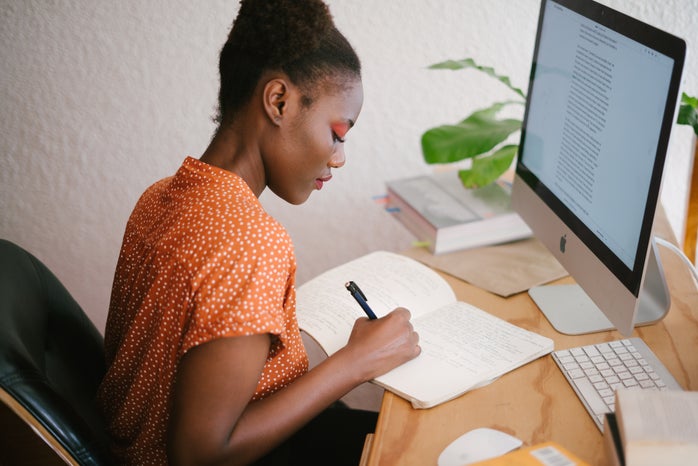 Black girl at computer desk writing in journal write natural work corporate african