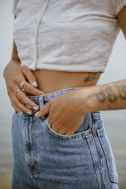 person with tattoos poses with their hand in their pocket