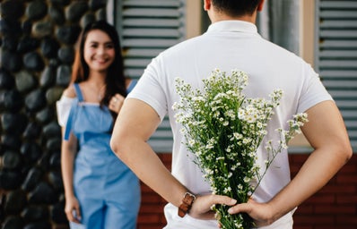 guy hiding flowers behind his back from girlfriend