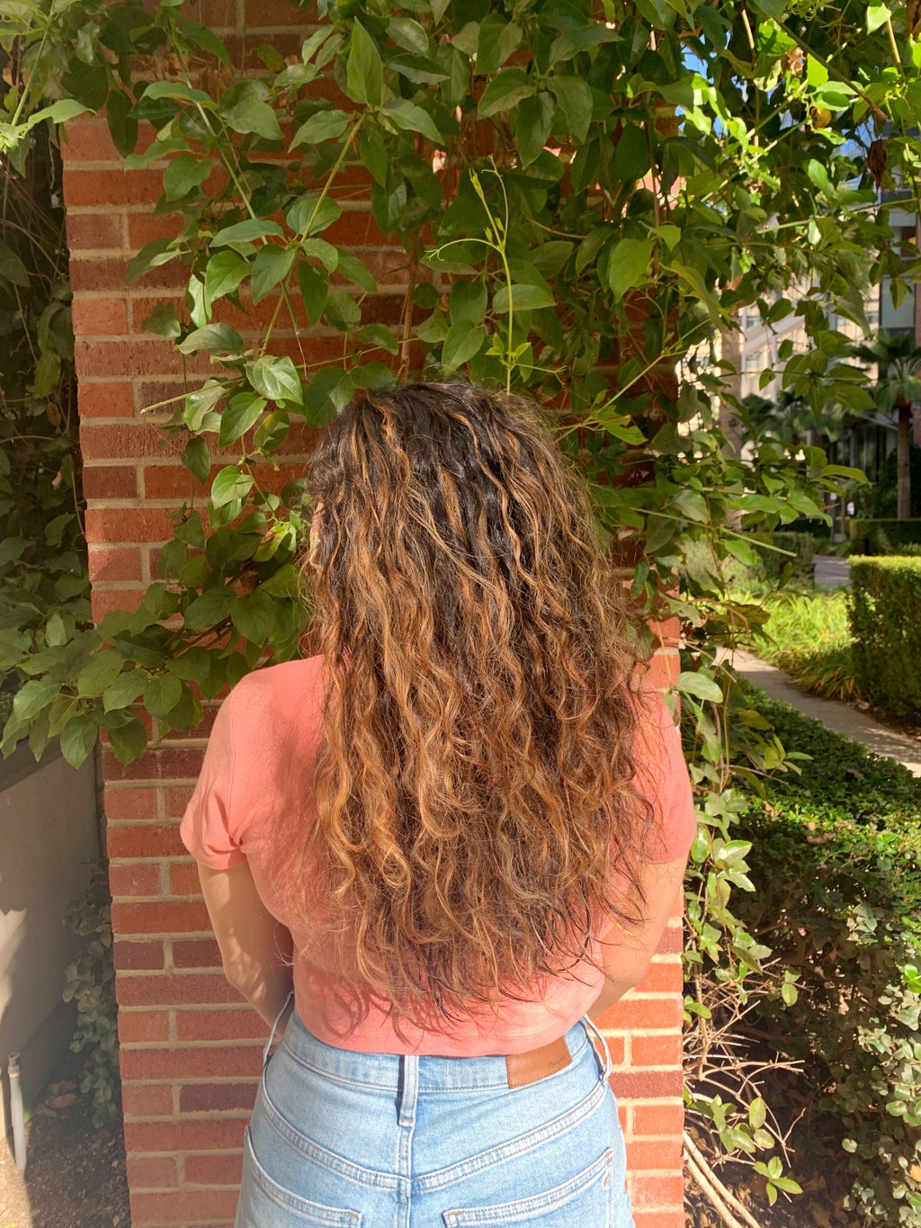 A woman stands by a wall with her back facing the camera.