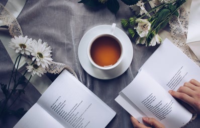 person reading poetry books next to tea and flowers