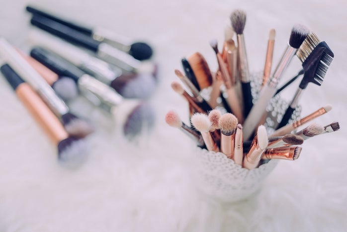 cup of makeup brushes with more brushes laying beside it on the table